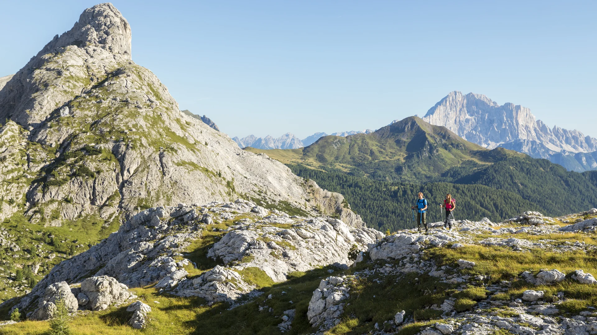 Bilder aus Arabba des Chalet Barbara Zwei Wanderer auf felsigem Pfad in grüner Berglandschaft bei klarem Himmel
