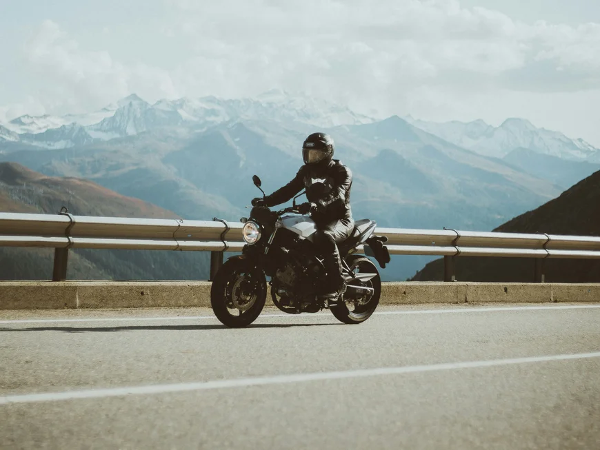 Motorcyclist in black gear riding on mountain road with snowy mountains in background