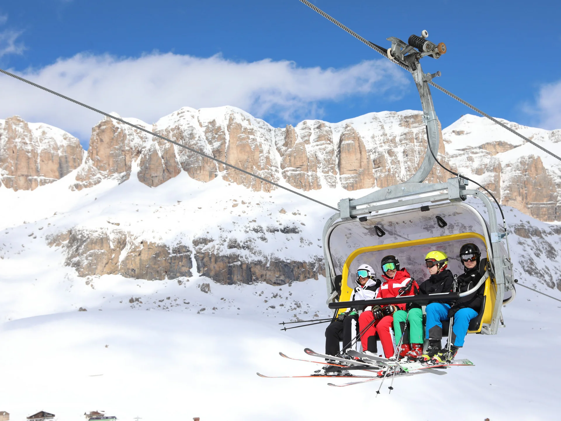 Four skiers on chairlift with snowy mountains in background