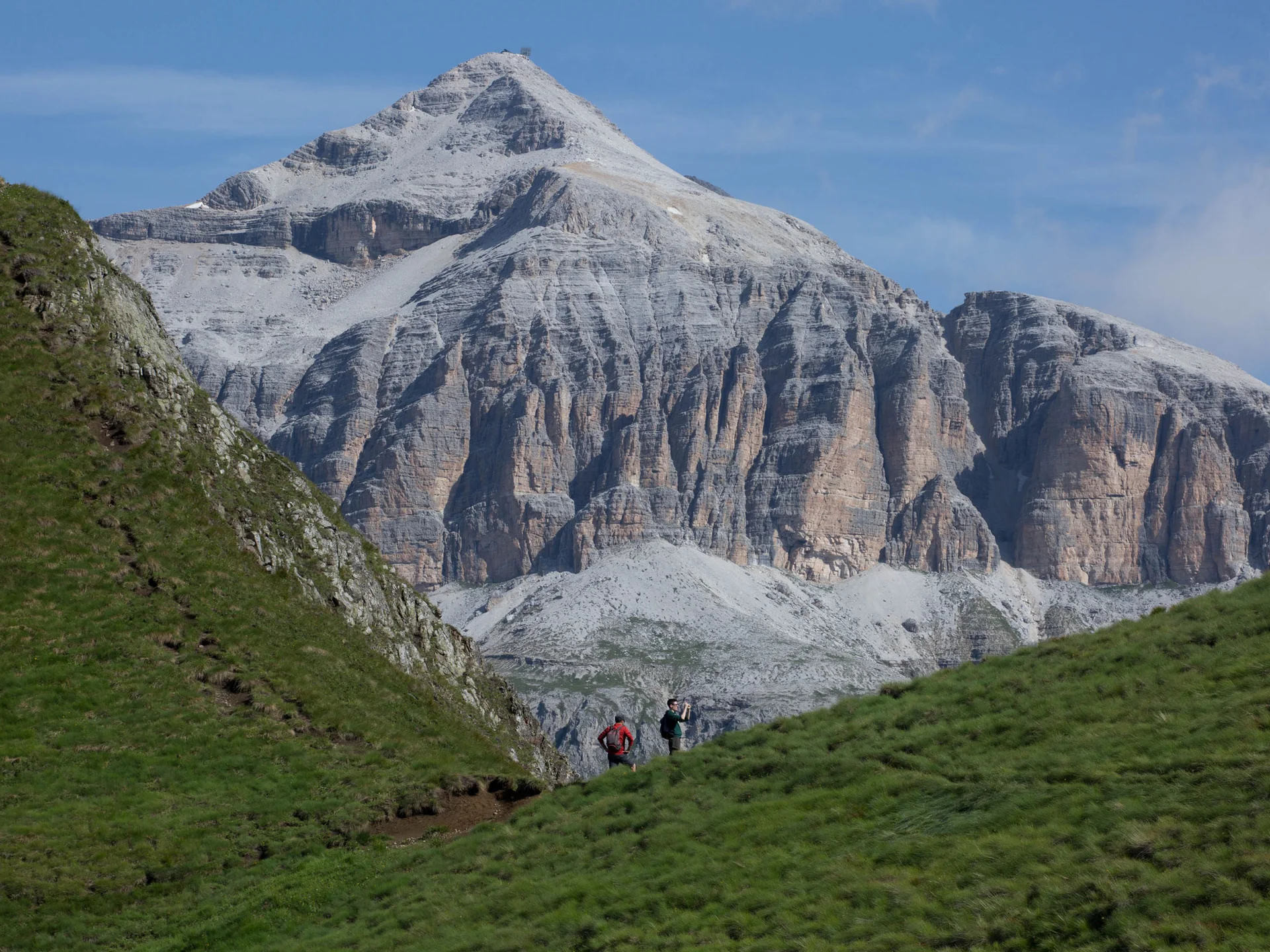 Rocky mountain with two hikers on a green trail