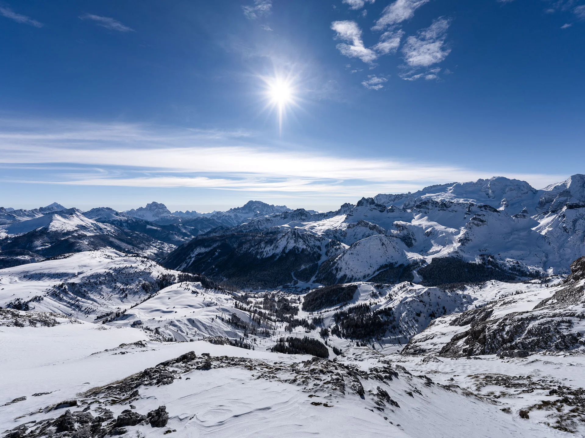 Snow-covered mountain landscape with bright sun and partly cloudy sky