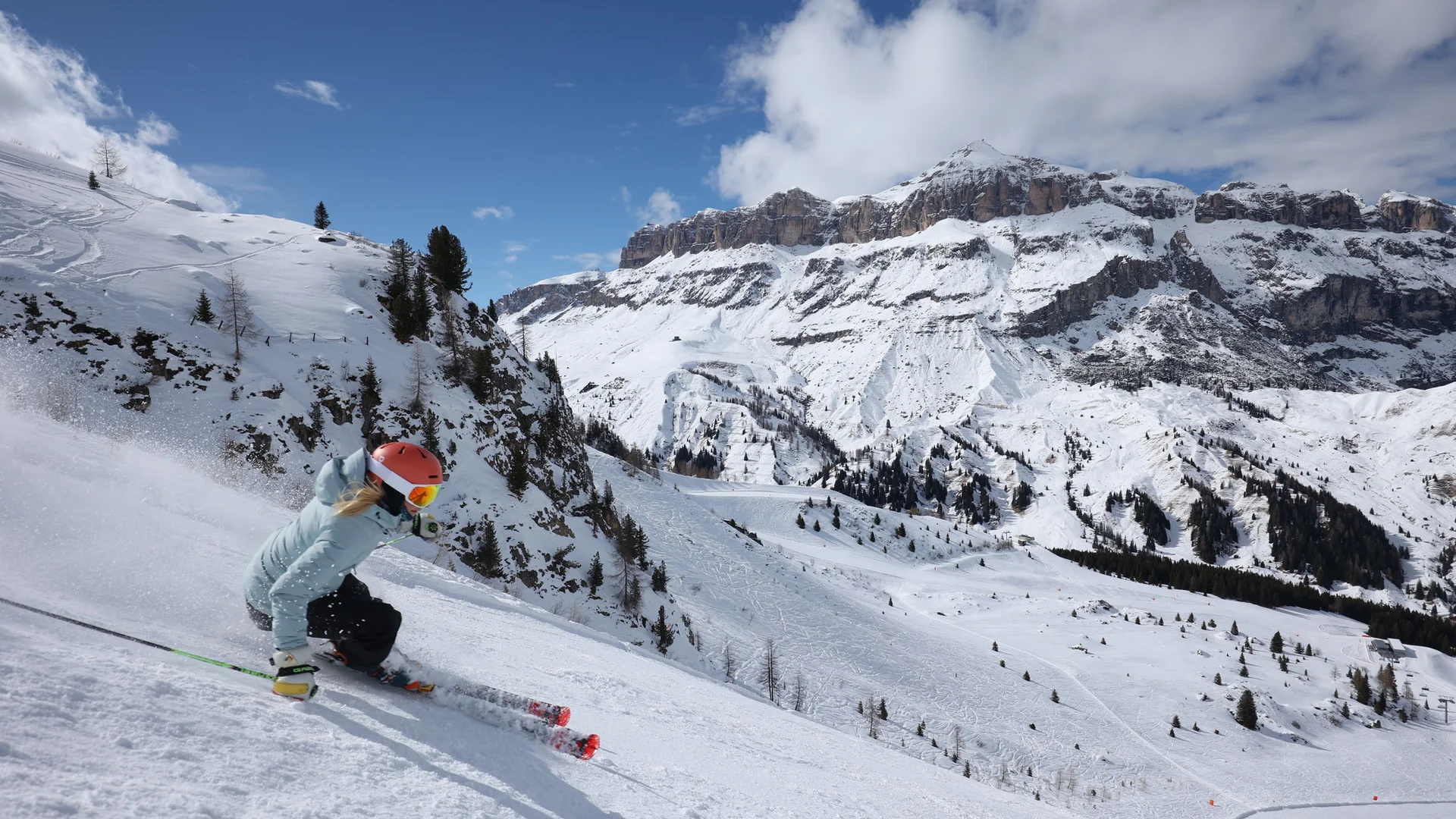 Bilder aus Arabba des Chalet Barbara Skifahrer mit rotem Helm auf verschneiter Piste vor Bergkulisse