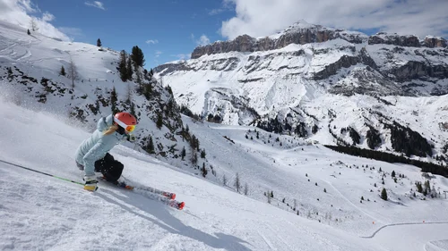 Accessibility Skier wearing red helmet skiing down snowy slope with mountains in background