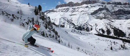 Skifahrer mit rotem Helm auf verschneiter Piste vor Bergkulisse
