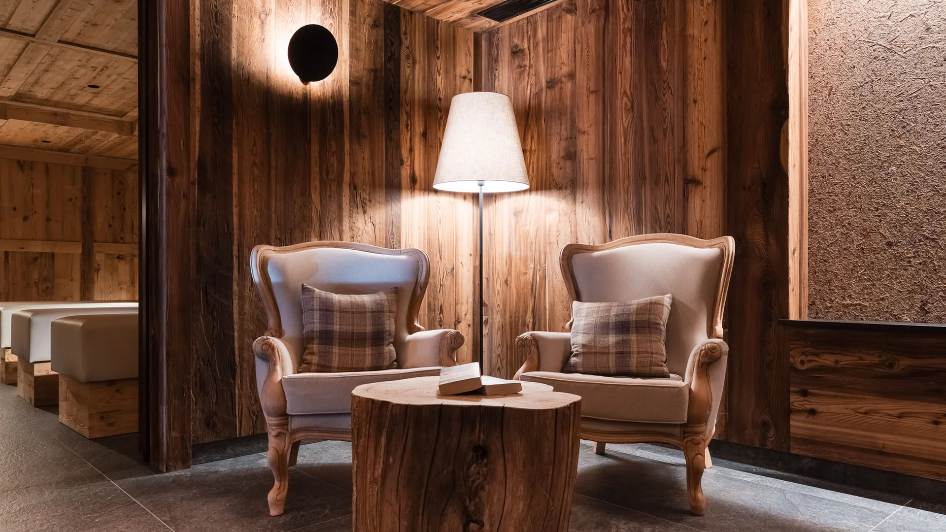 Bilder aus Arabba des Chalet Barbara Zwei Sessel mit karierten Kissen und Holztisch in einem Raum mit Holzvertäfelung