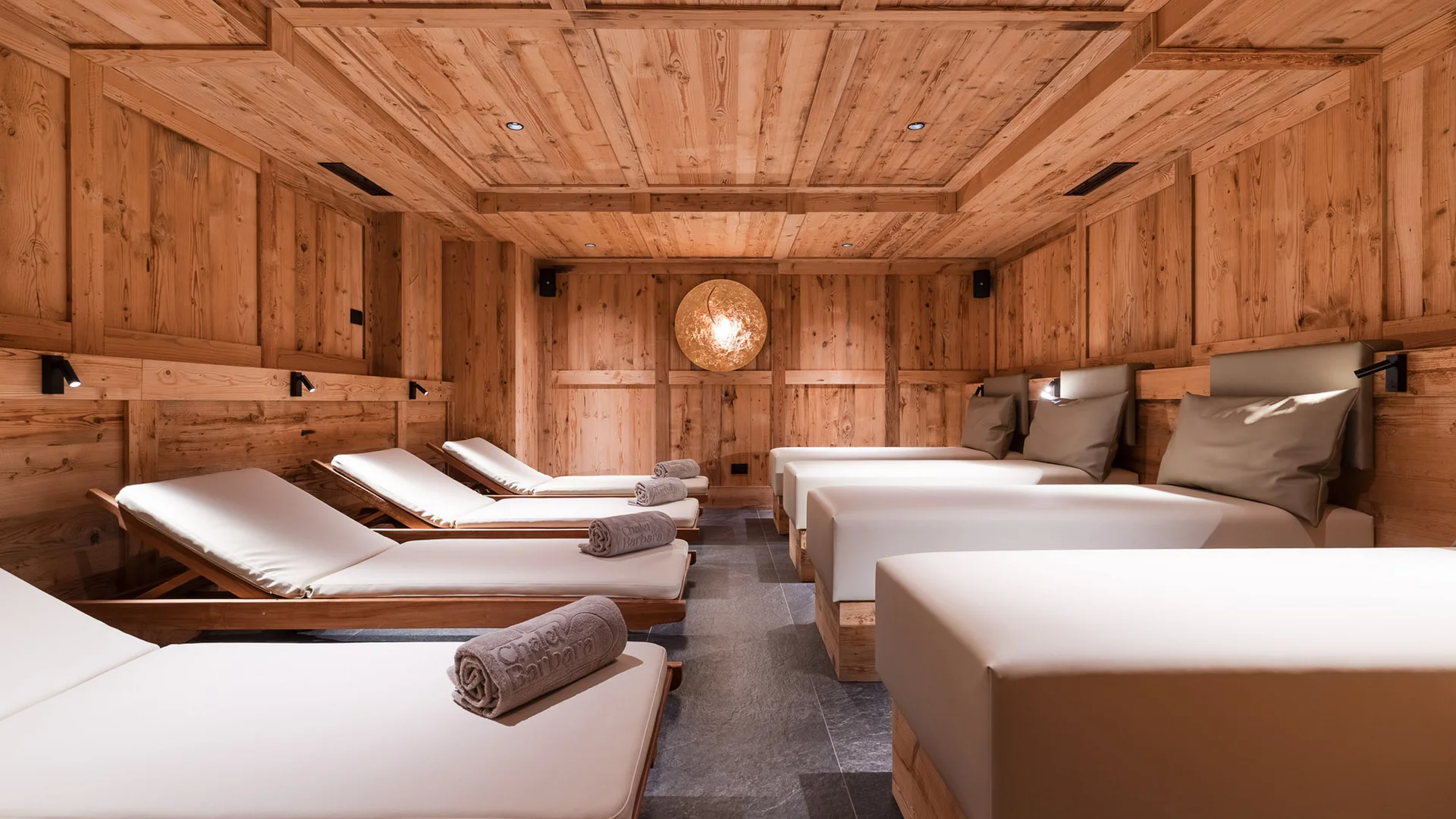 Bilder aus Arabba des Chalet Barbara Entspannungsraum aus Holz mit gepolsterten Liegen und gerollten Handtüchern