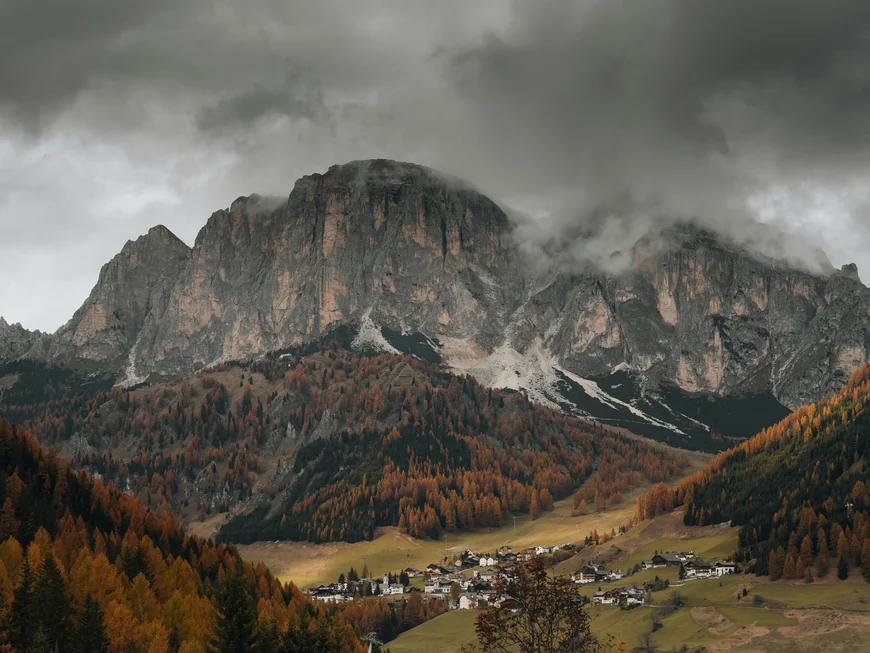 Village at the foot of rocky mountains with cloudy sky and autumn trees