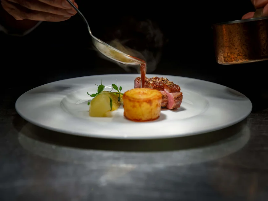 Koch gießt heiße Sauce auf Gourmet-Teller mit Fleisch und Beilagen