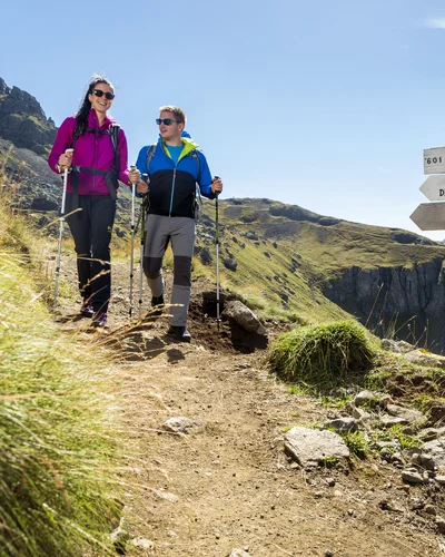 Couple hiking on mountain trail with directional signs and rocky landscape