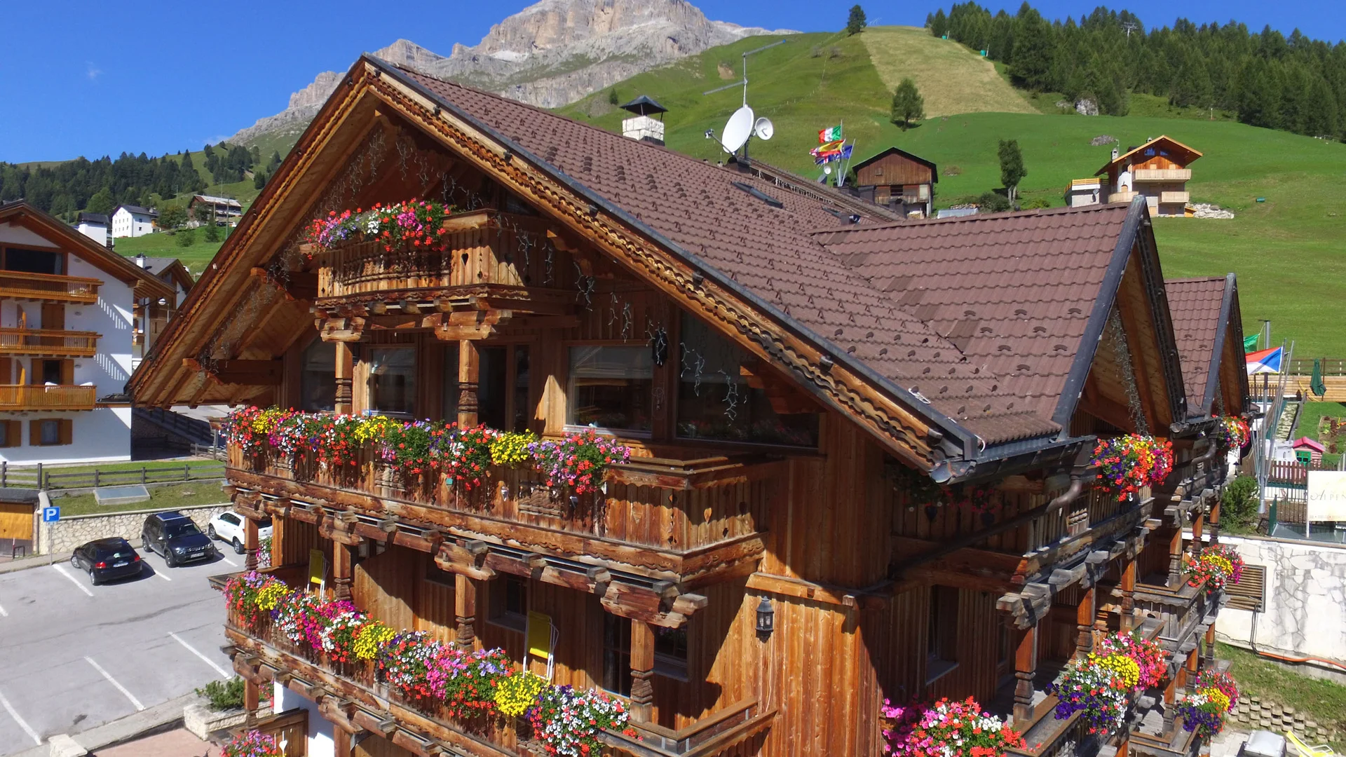 Bilder aus Arabba des Chalet Barbara Holzhaus mit blumengeschmückten Balkonen in sonniger Berglandschaft
