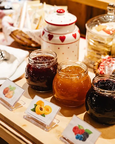 Jars of assorted jams with labels and cutlery on a wooden table