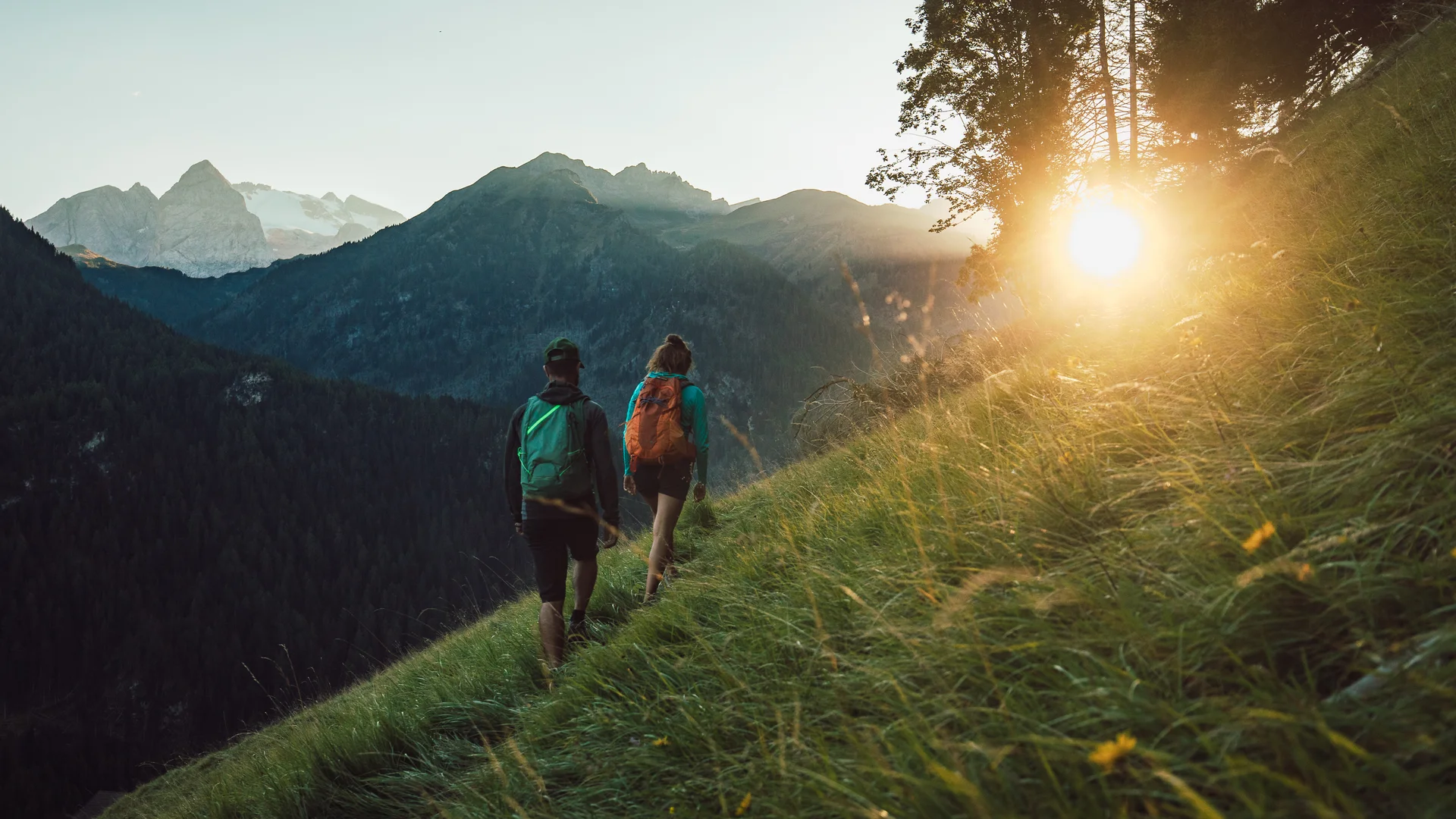 Bilder aus Arabba des Chalet Barbara Zwei Wanderer mit Rucksäcken auf einem grasbewachsenen Pfad bei Sonnenuntergang in den Bergen