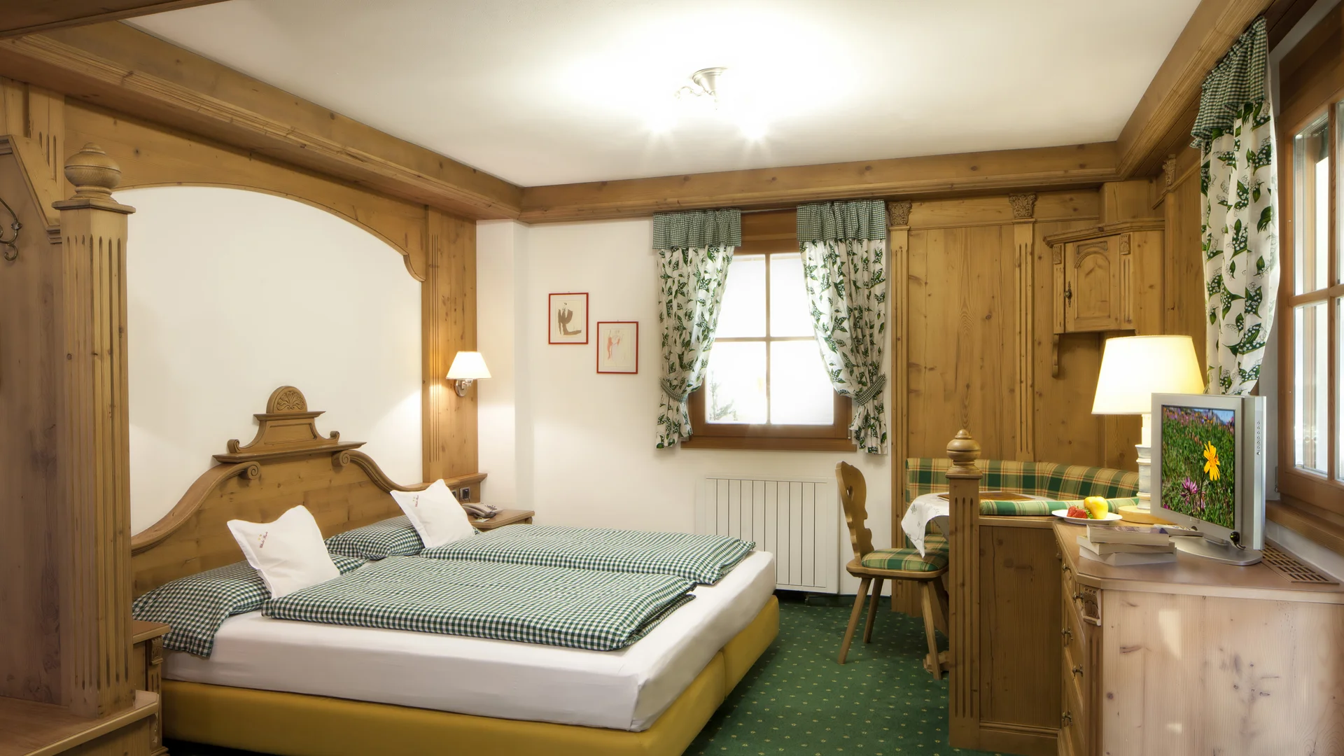 Bilder aus Arabba des Chalet Barbara Hotelzimmer mit Doppelbett, Holzmöbeln und grünen karierten Vorhängen