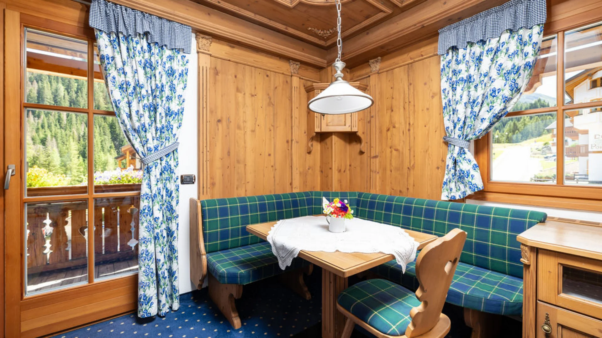 Bilder aus Arabba des Chalet Barbara Holzeckbank mit blau karierten Polstern und blauen Vorhängen
