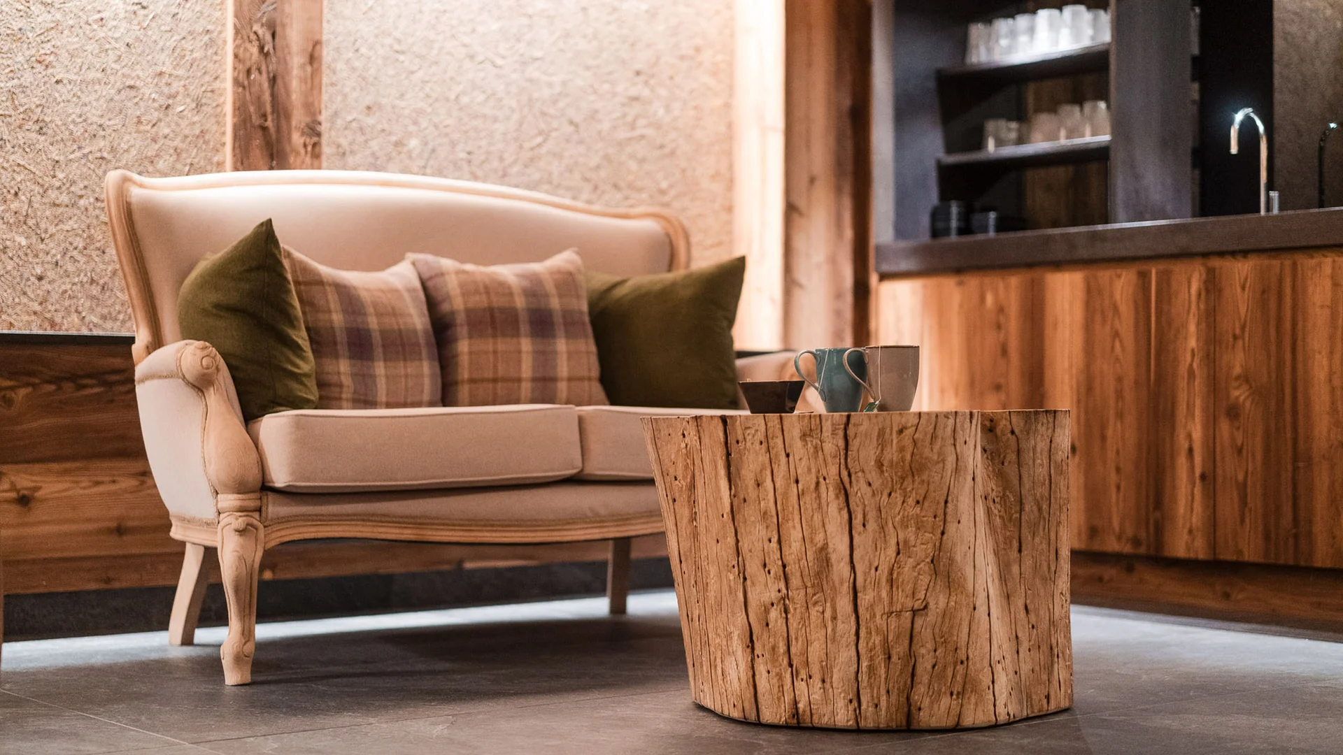 Dein Chalet-Hotel mit Wellness in den Dolomiten Beiges Sofa mit Kissen und rustikalem Holztisch im Wohnzimmer