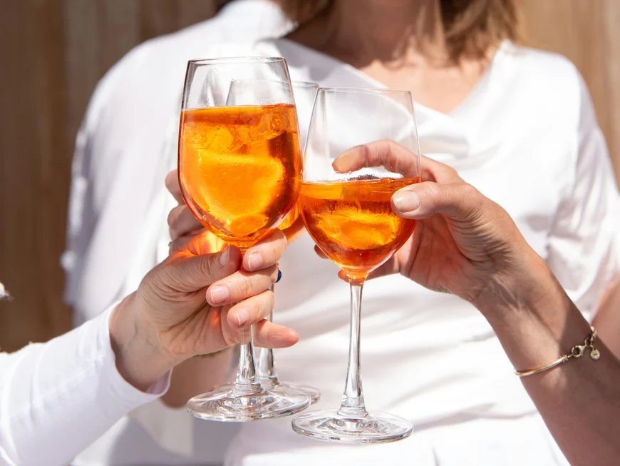 Drei Personen stoßen mit Gläsern voller orangenem Cocktail mit Eis an