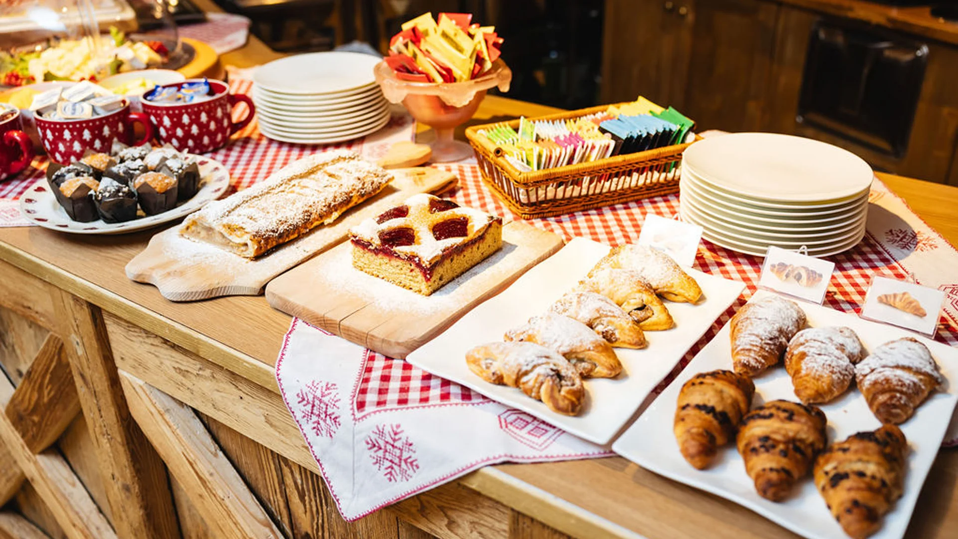 Bilder aus Arabba des Chalet Barbara Buffet mit Croissants, Kuchen und Muffins auf rustikalem Holztisch