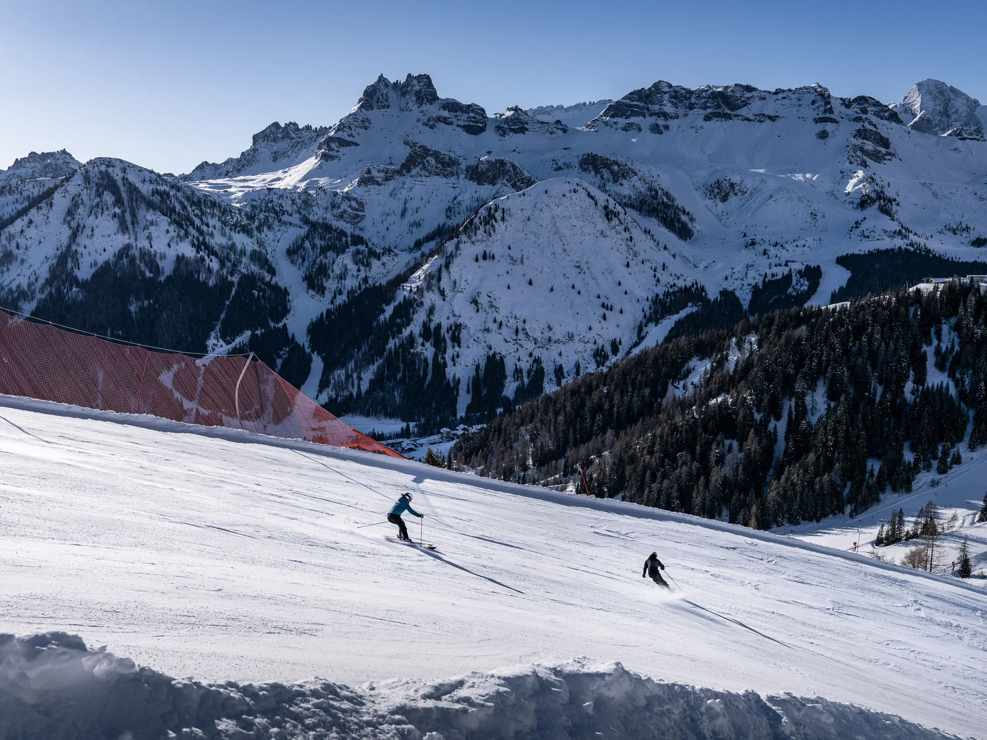 Skiers descending a snowy slope with snow-covered mountains in the background