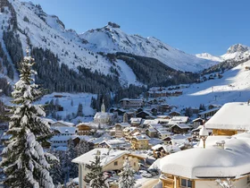Snow-covered village in the mountains with trees and houses under a clear blue sky