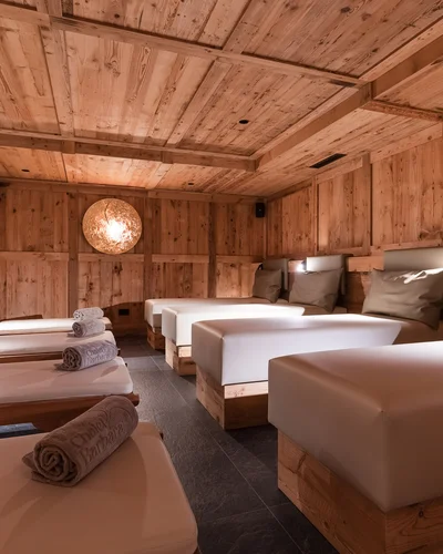 Dein Chalet-Hotel mit Wellness in den Dolomiten Entspannungsraum aus Holz mit gepolsterten Liegen und gerollten Handtüchern