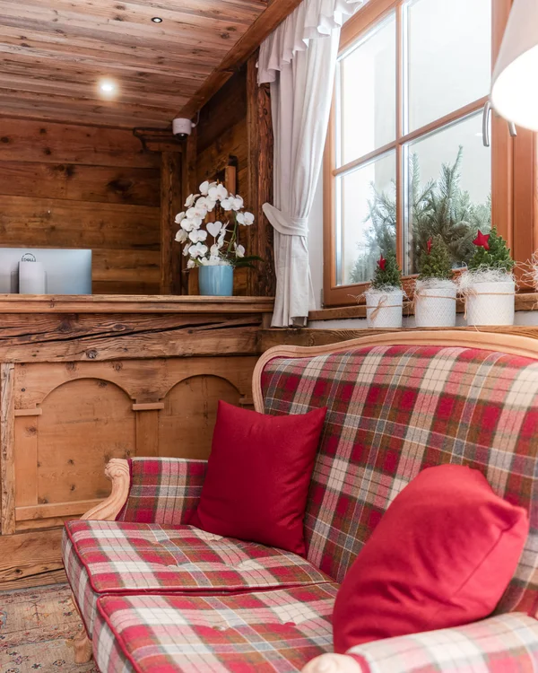The story of our chalet in Arabba Rustic interior with red plaid sofa and red cushions next to a window