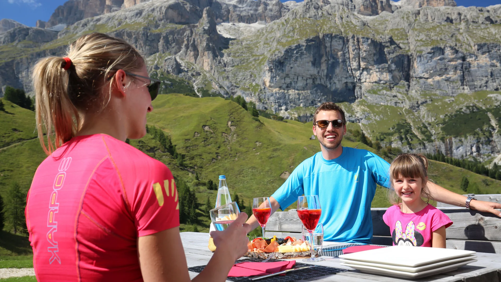 Bilder aus Arabba des Chalet Barbara Familie isst draußen mit Bergen im sonnigen Hintergrund