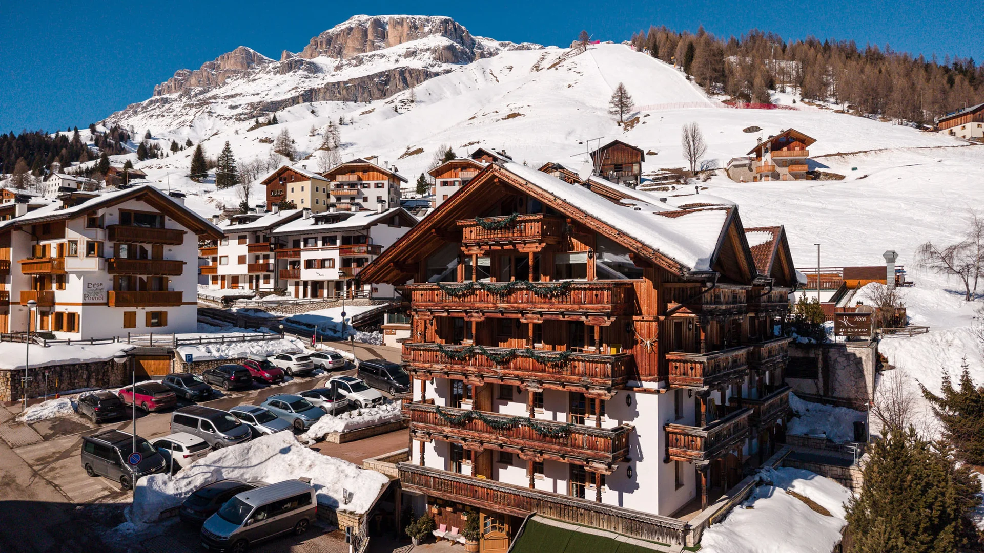 Bilder aus Arabba des Chalet Barbara Holzhotel mit blumengeschmückten Balkonen vor verschneiten Bergen