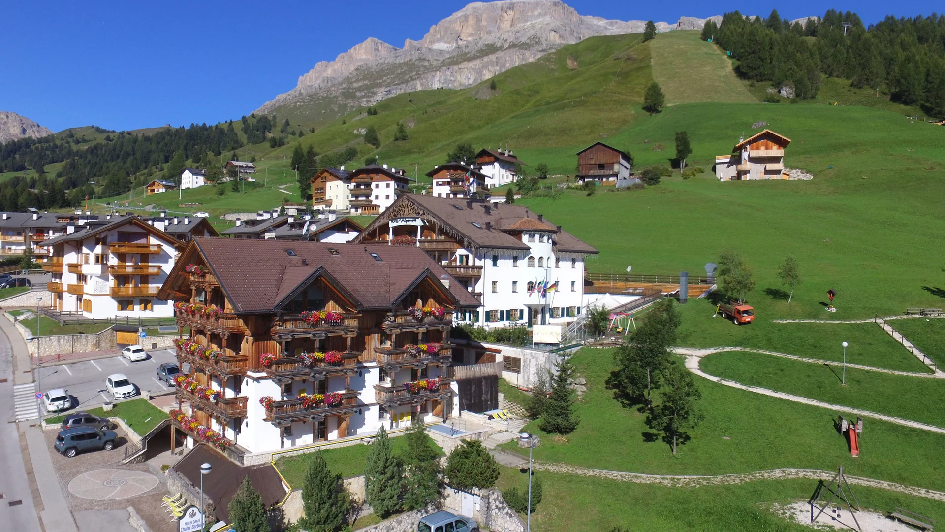 Bilder aus Arabba des Chalet Barbara Hotel mit blumengeschmückten Balkonen in einem Bergdorf mit grünen Wiesen und Bergen