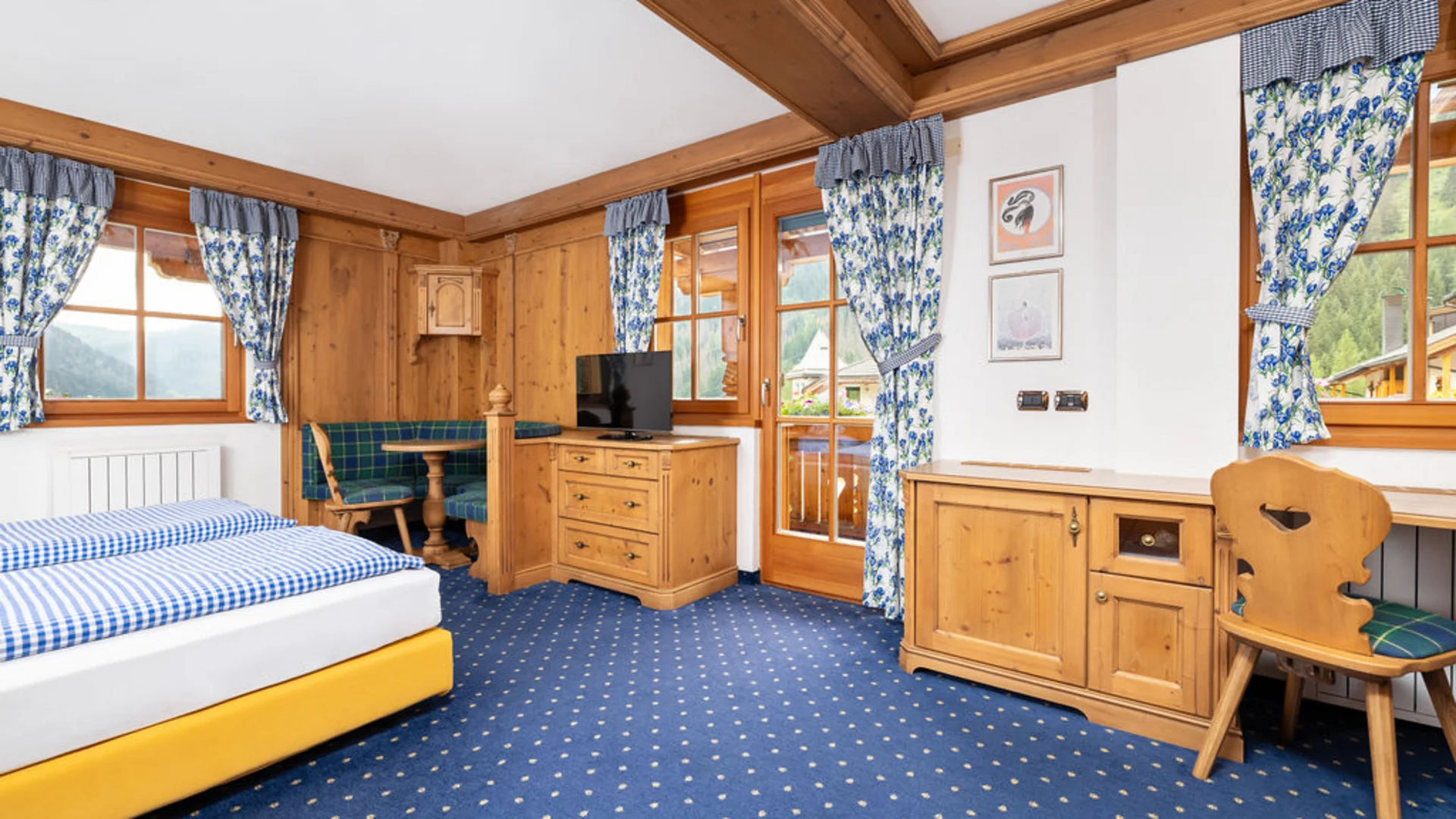 Bilder aus Arabba des Chalet Barbara Hotelzimmer mit Holzmöbeln, Bett, Fernseher und blauen Blumenvorhängen