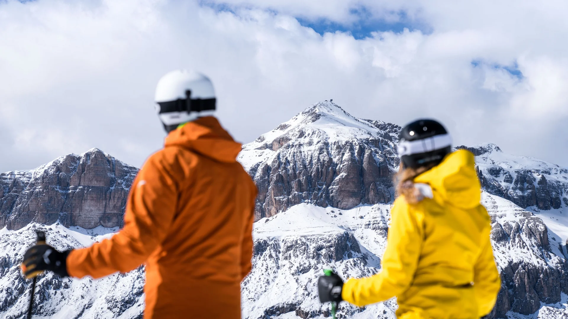 Bilder aus Arabba des Chalet Barbara Zwei Skifahrer in orange und gelb blicken auf schneebedeckte Berge