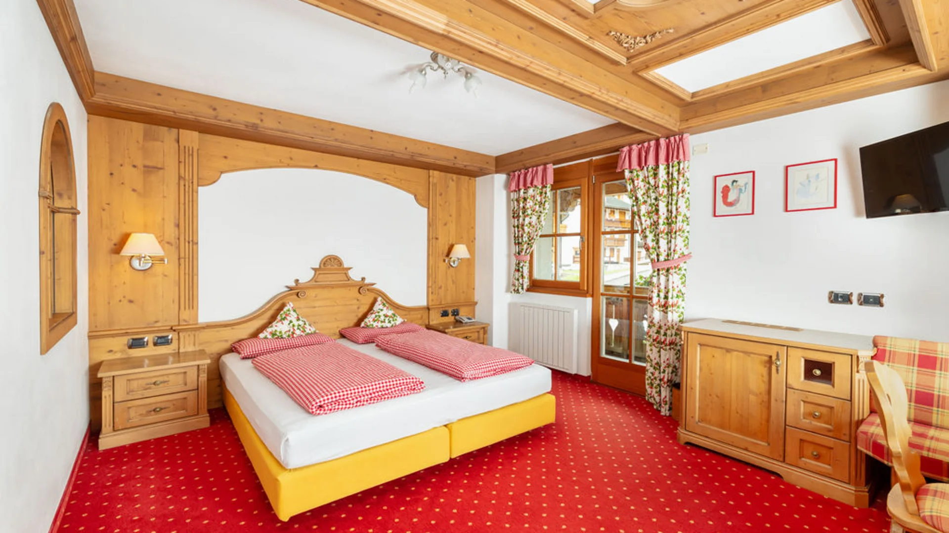 Bilder aus Arabba des Chalet Barbara Schlafzimmer mit Doppelbett, Holzmöbeln und rotem Teppichboden