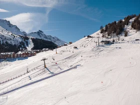 Snow-covered ski slope with chairlifts and mountains in the background