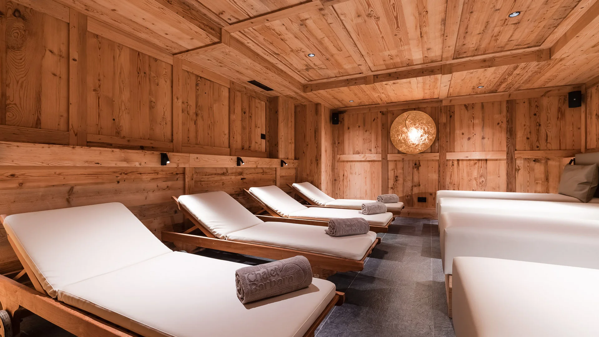 Dein Chalet-Hotel mit Wellness in den Dolomiten Entspannungsraum aus Holz mit gepolsterten Liegen und gerollten Handtüchern