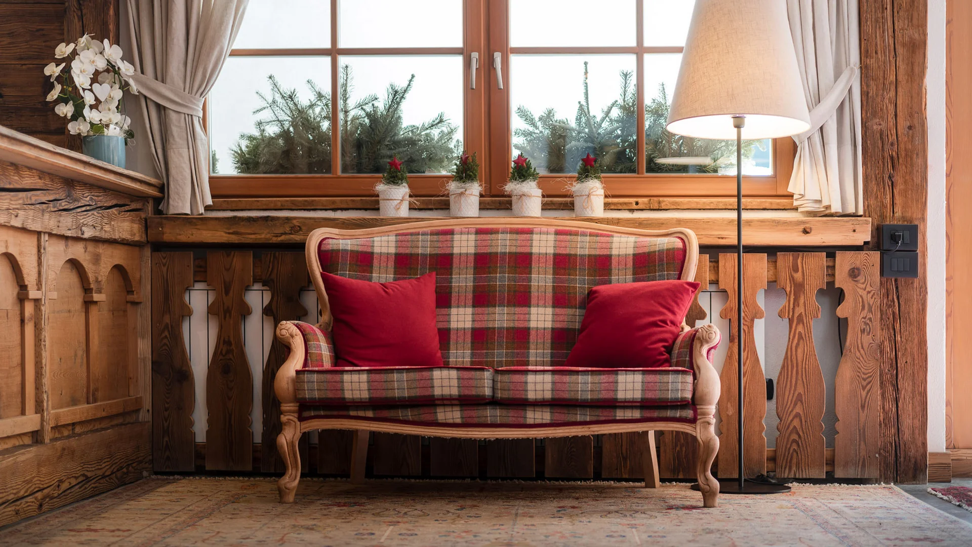 Bilder aus Arabba des Chalet Barbara Karierter Sofa mit roten Kissen in rustikalem Zimmer mit Lampe und Fenster