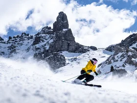 Skier in yellow jacket skiing on snowy slope with rocky mountains behind