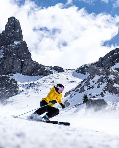 Skier in yellow jacket skiing on snowy slope with rocky mountains behind